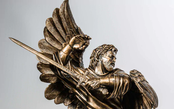 HD desktop wallpaper featuring a detailed man-made angel statue holding a spear with wings spread against a plain background.