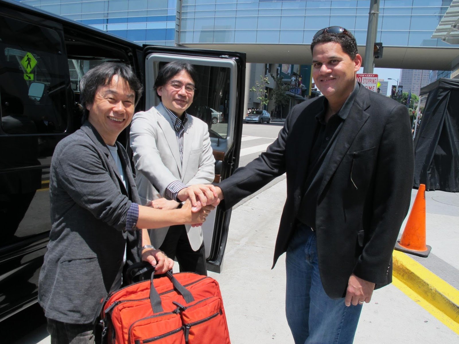 HD desktop wallpaper featuring Shigeru Miyamoto shaking hands with two other individuals beside a vehicle.