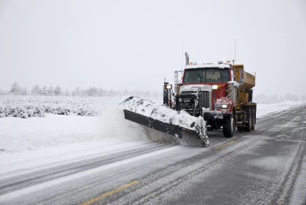 HD desktop wallpaper of a snowplow vehicle clearing snow with a large plow attachment on a wintry road.
