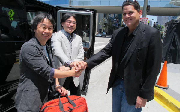 HD desktop wallpaper featuring Shigeru Miyamoto shaking hands with two other individuals beside a vehicle.