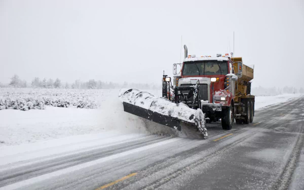 HD desktop wallpaper of a snowplow vehicle clearing snow with a large plow attachment on a wintry road.