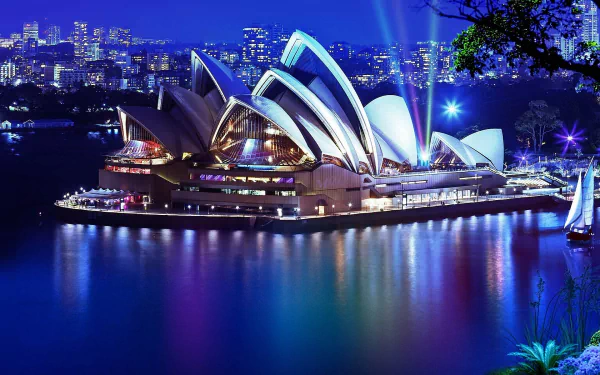 HD desktop wallpaper showcasing the Sydney Opera House illuminated at night, set against the city skyline and calm waters of Sydney Harbor.