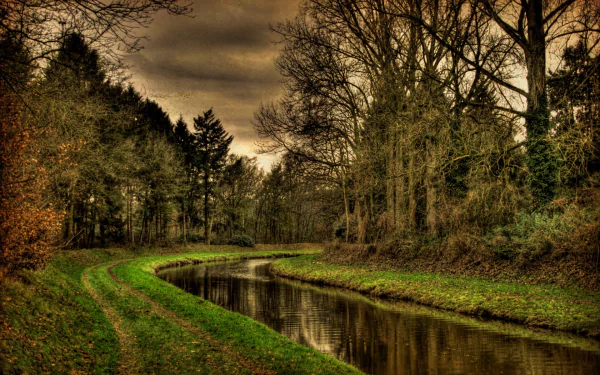 A serene river meanders through lush greenery and trees under a dramatic sky, creating a tranquil nature scene for a vibrant HD desktop wallpaper.