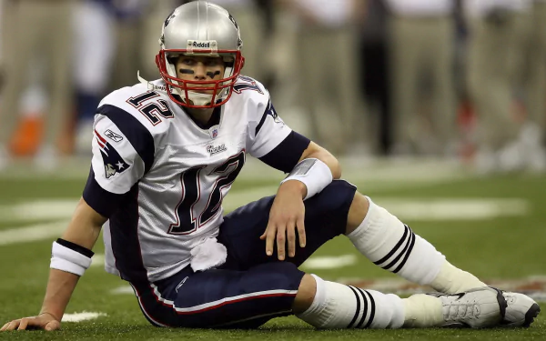 HD desktop wallpaper featuring a New England Patriots player in full uniform sitting on the football field during a game.