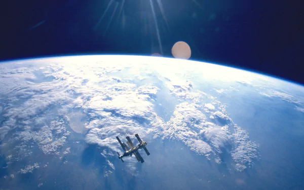 HD desktop wallpaper showing Earth from space with sunlight illuminating cloud-covered continents and a space station orbiting above the planet.
