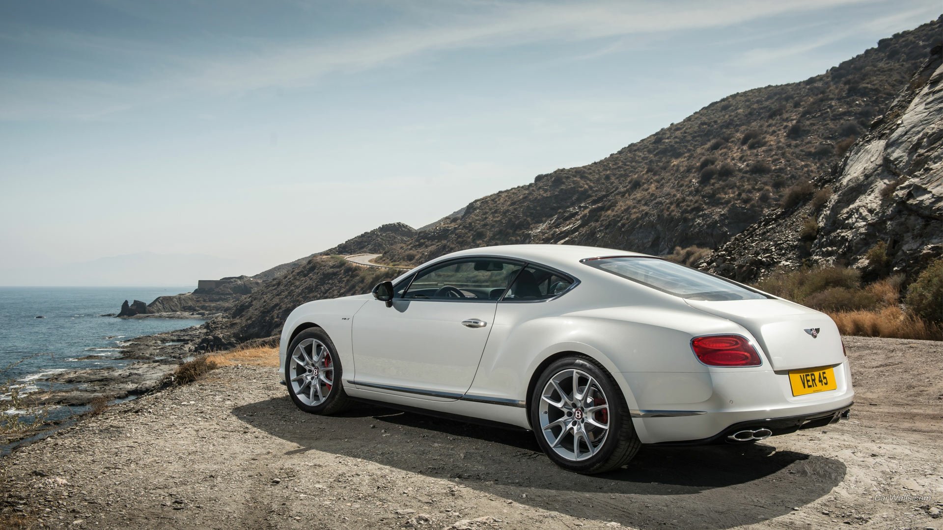 White Bentley Continental GT V8 parked on a coastal road by cliffs and sea — HD PC desktop wallpaper background.