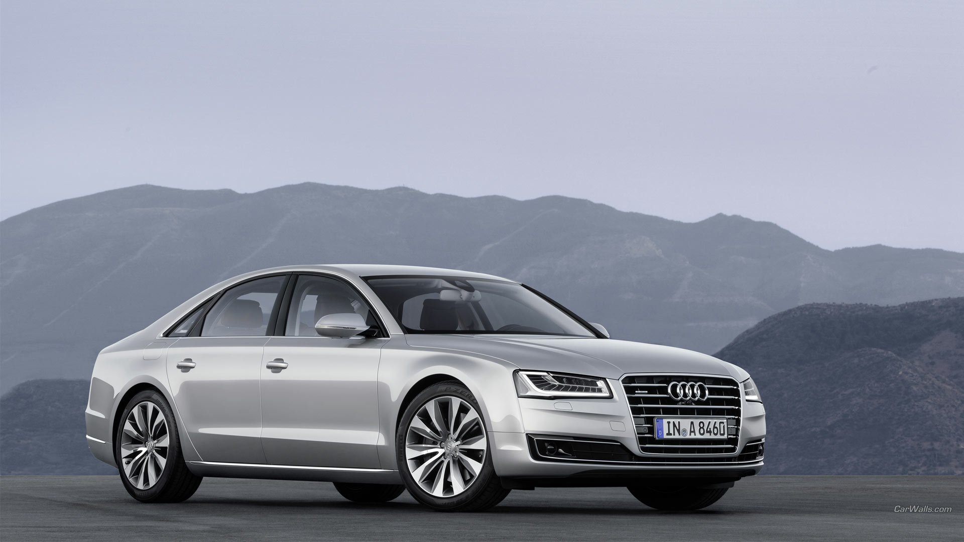A sleek Audi A8 stands poised against a mountainous backdrop, showcasing its elegant design in this high-definition desktop wallpaper.