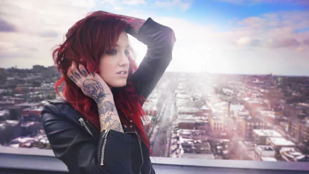 HD desktop wallpaper featuring a red-haired woman showcasing detailed tattoos on her hand and forearm, set against a sunlit cityscape background.