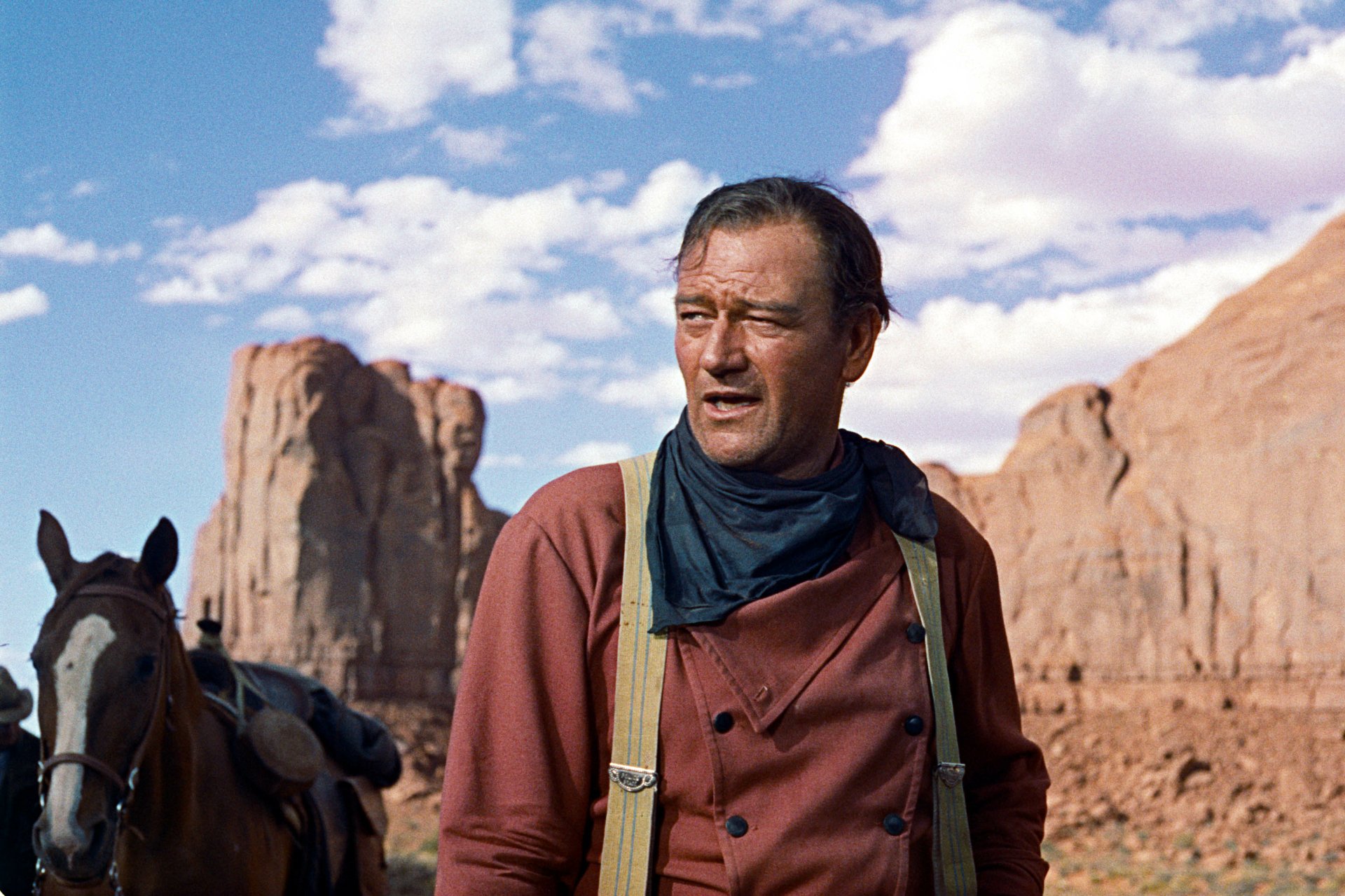 Rugged man in Western shirt and neckerchief with saddled horse and red rock buttes — still from the movie The Searchers, 2K Quad HD PC desktop wallpaper.