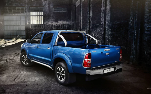 HD desktop wallpaper featuring a blue Toyota Hilux parked in an urban, industrial setting with dramatic lighting highlighting the vehicle.