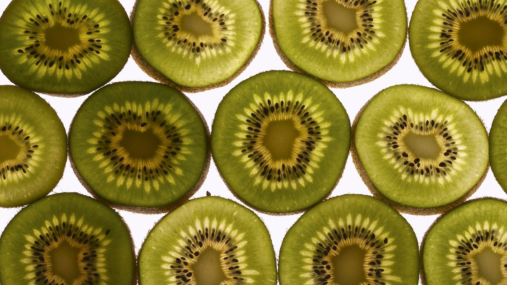 Close-up pattern of sliced kiwi fruit filling the frame — vibrant green food texture, 2K Quad HD PC desktop wallpaper background.