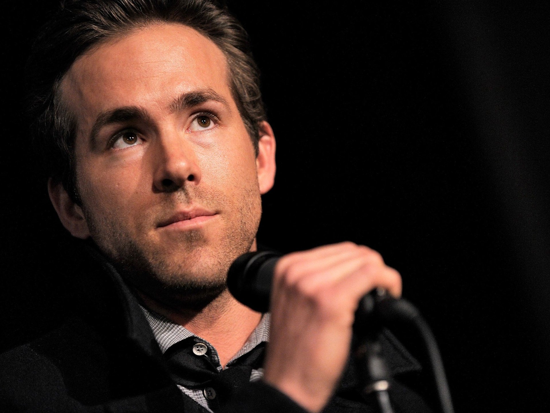 HD desktop wallpaper featuring a close-up of celebrity Ryan Reynolds speaking into a microphone against a dark background.
