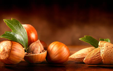 Close-up of various nuts, including hazelnuts and almonds, arranged artistically with green leaves, set against a warm, blurred background. HD desktop wallpaper for food lovers.