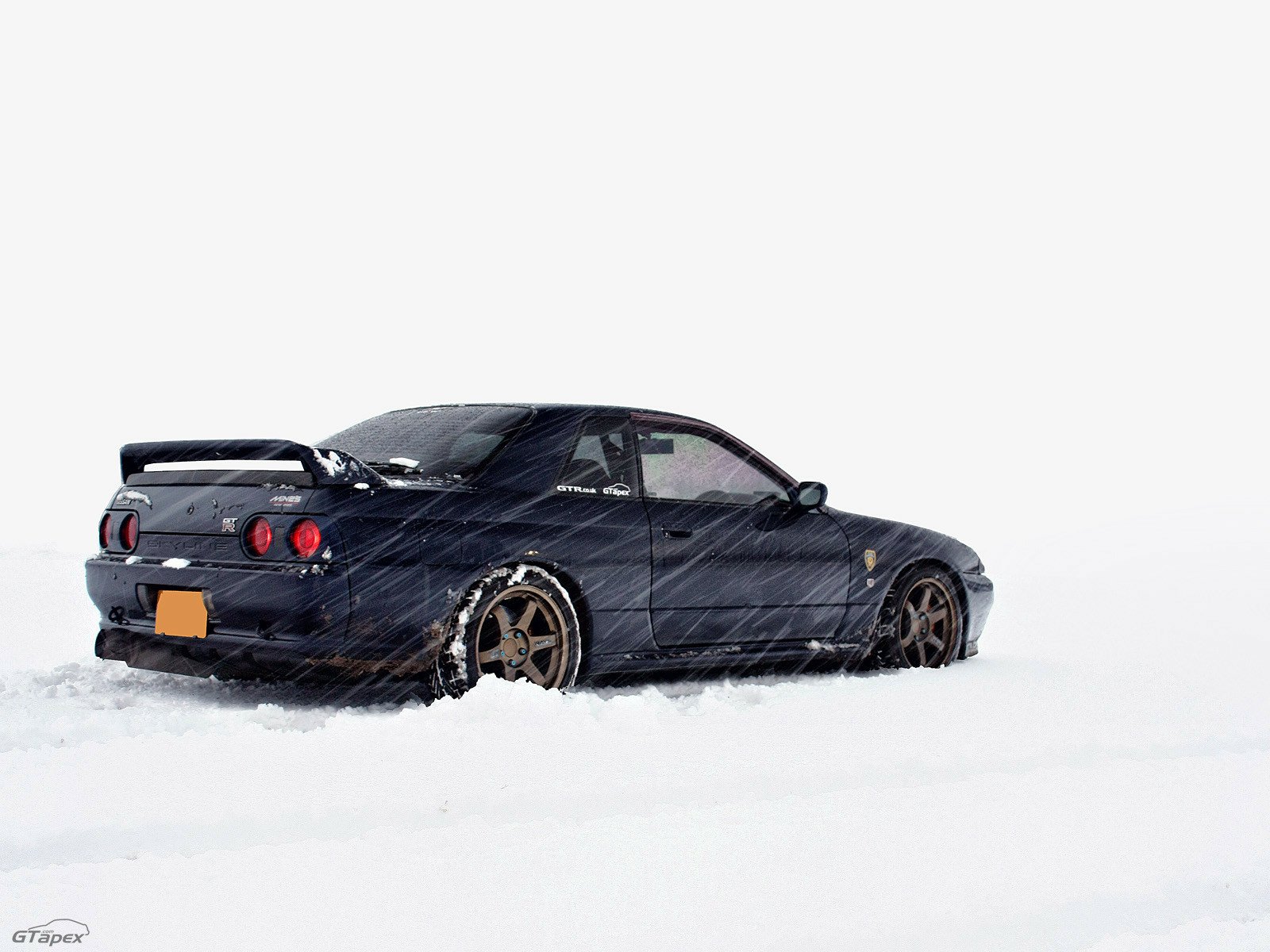 Nissan Skyline coupe in falling snow on a clean white background — HD PC desktop wallpaper of a sporty vehicle.