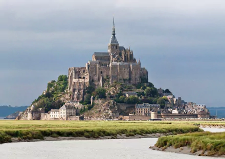 HD desktop wallpaper of Mont Saint-Michel, showcasing its iconic religious architecture perched on a rocky island surrounded by tidal flats under a cloudy sky.