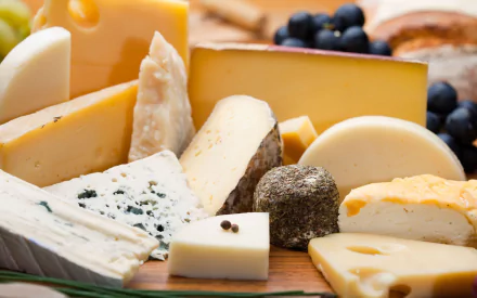 HD PC desktop wallpaper featuring a close-up of assorted cheeses arranged on a wooden board with dark grapes in the background.