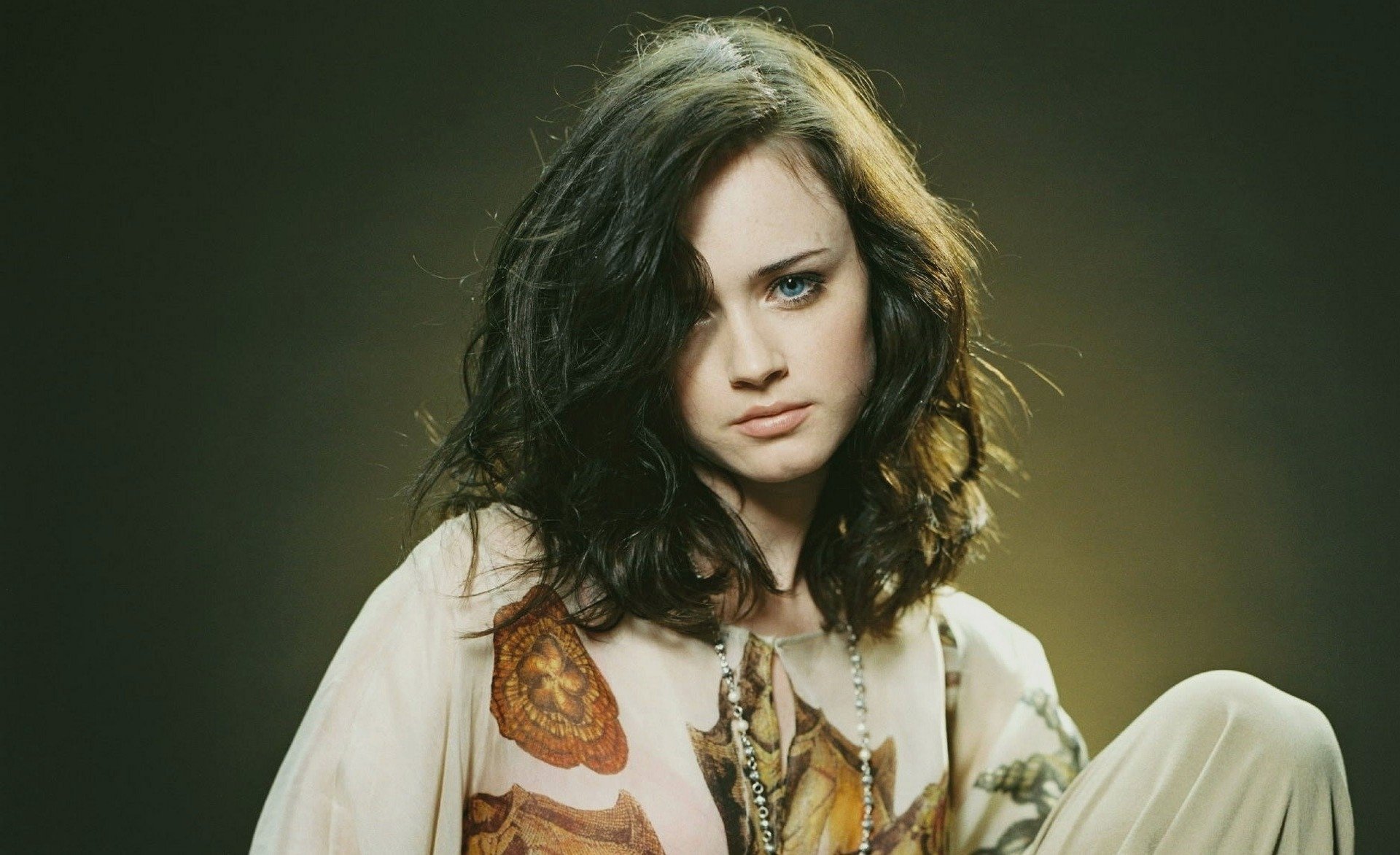 HD desktop wallpaper featuring celebrity Alexis Bledel with dark wavy hair, wearing a patterned blouse against a muted dark background.
