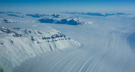 Aerial view of McMurdo Station man-made outpost beside vast Antarctic ice plains and ridged glaciers, snow-clad mountains on the horizon — 4K Ultra HD PC desktop wallpaper.