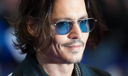 Johnny Depp smiles while wearing stylish sunglasses, showcasing his confident look in this HD desktop wallpaper featuring the well-known actor.