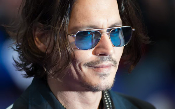 Johnny Depp smiles while wearing stylish sunglasses, showcasing his confident look in this HD desktop wallpaper featuring the well-known actor.