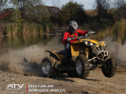 HD PC desktop wallpaper of a rider in a red jacket on a yellow Can-Am ATV kicking up dirt along a lakeside trail, dynamic off-road action shot