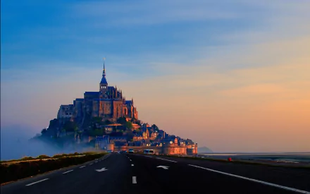 Scenic HD wallpaper of Mont Saint-Michel at sunset, showcasing its iconic religious architecture surrounded by mist and a clear sky.