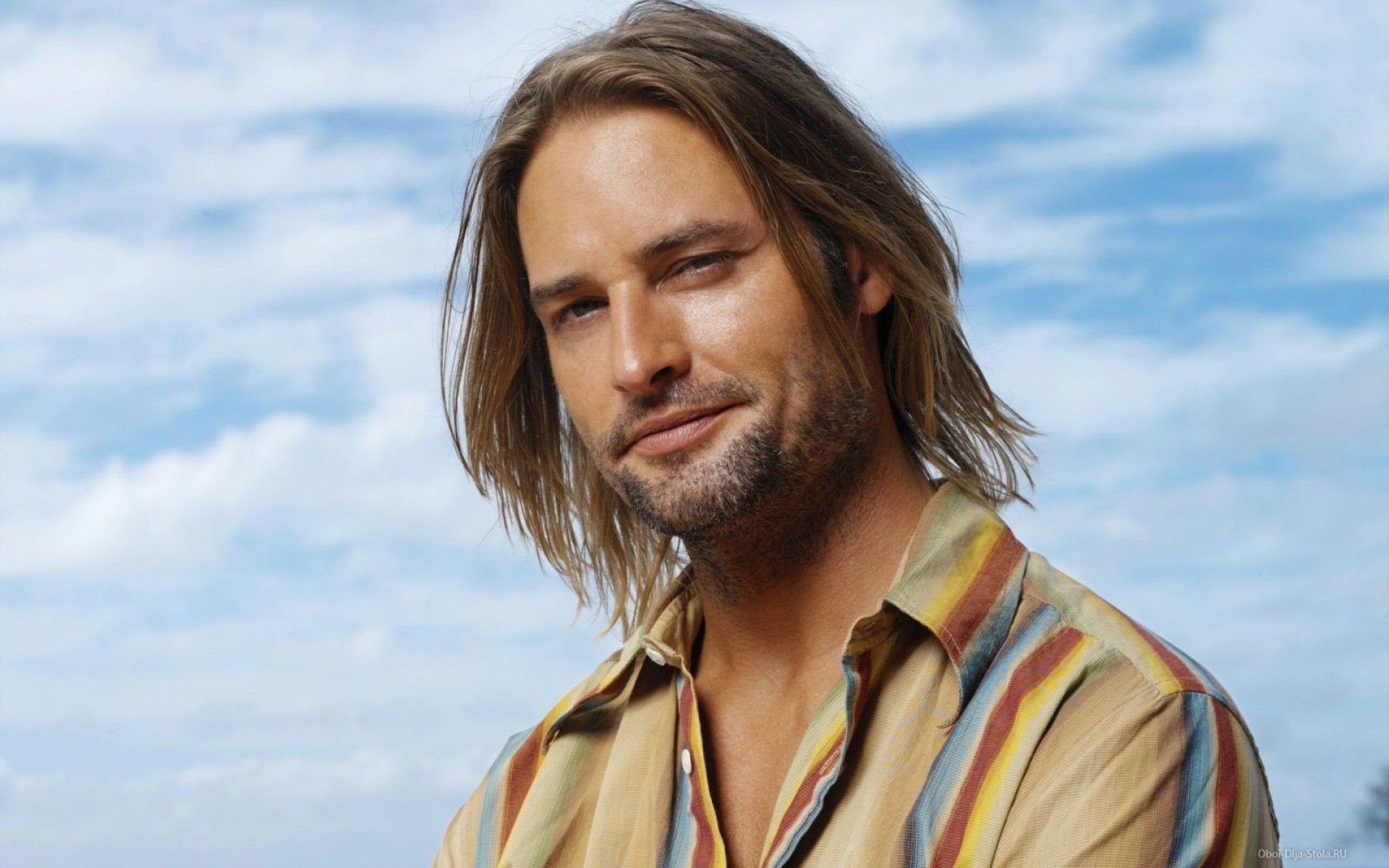 HD PC desktop wallpaper of a smiling long-haired male celebrity actor in a striped shirt posed against a bright blue sky background.