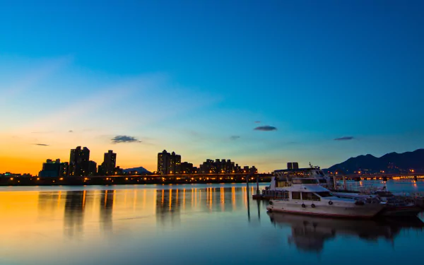 A serene sunset view of Dadaocheng, Taipei, showcasing shimmering water reflections and silhouetted buildings against a vibrant sky. Man-made beauty meets natural tranquility.