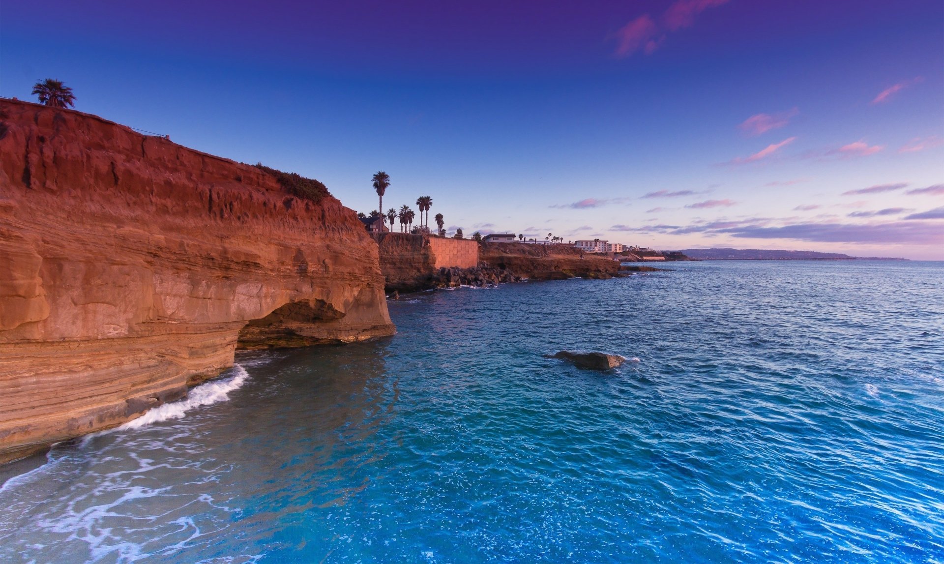 HD desktop wallpaper showcasing a vibrant nature scene with rugged cliffs overlooking a calm, expansive ocean under a colorful twilight sky.