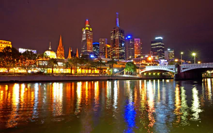 Night view of Melbourne's illuminated skyscrapers reflecting on the Yarra River, showcasing the vibrant cityscape of Australia in HD.