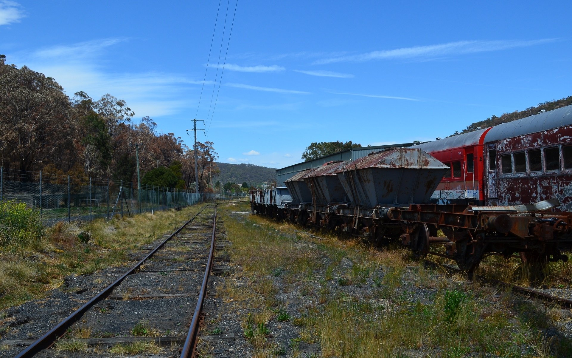 HD desktop wallpaper of a rustic Lithgow railroad featuring weathered hopper cars alongside old train vehicles under a clear blue sky.