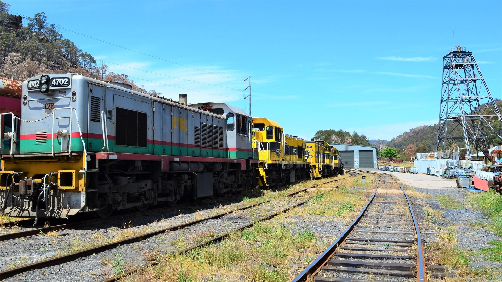 Lithgow train and locomotives, rail vehicles parked on sidings beside tracks under a bright blue sky — 2K Quad HD PC desktop wallpaper background.