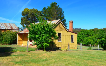 HD desktop wallpaper featuring an old yellow house surrounded by green trees under a clear blue sky in a serene outdoor setting.