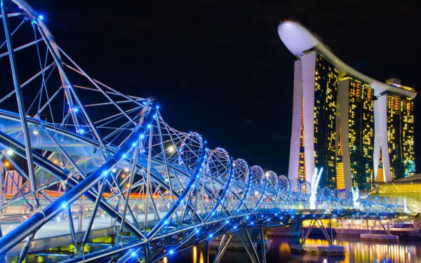 Night view of Singapore's Helix Bridge illuminated in blue, with the iconic Marina Bay Sands hotel glowing in the background.