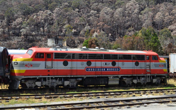 HD desktop wallpaper showing a red and silver Lithgow locomotive train parked on railway tracks with a forested hillside background.