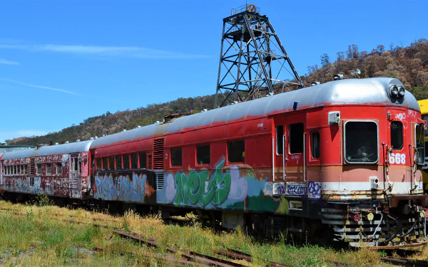 Graffiti-covered railcars stand on tracks in Lithgow, Australia, under a clear blue sky, captured in an HD desktop wallpaper showcasing vintage trains.
