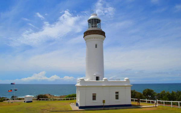 Norah Head Lighthouse stands tall against a bright sky with clouds on the horizon, featuring the Australian coastline in the background.