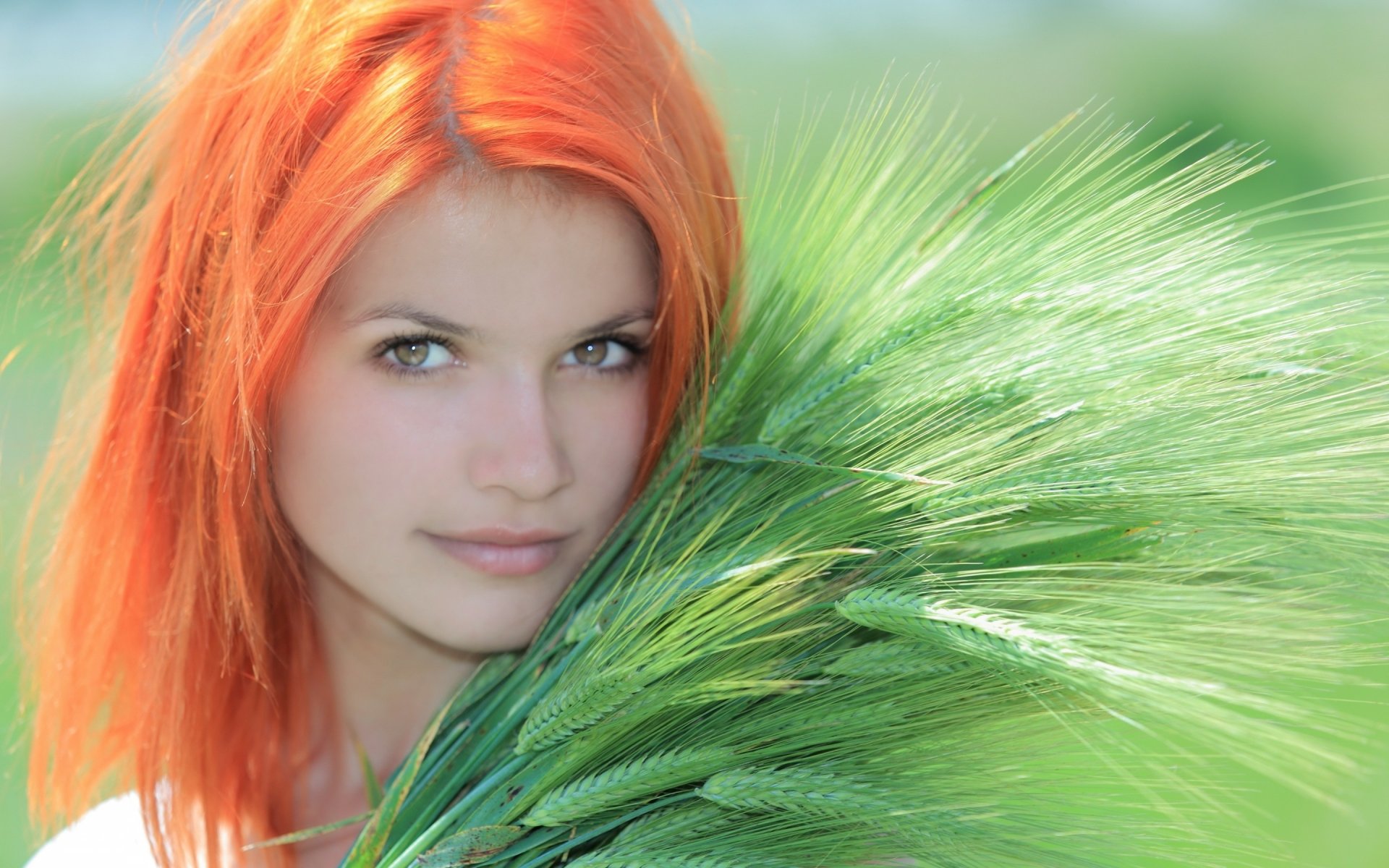 A high-definition desktop wallpaper featuring a woman with vibrant orange hair holding green foliage against a blurred natural background.