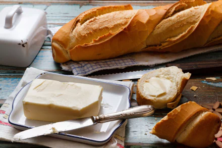 A delicious spread of butter on fresh bread, with a rustic setting featuring a loaf and a butter dish, creating a warm and inviting food-themed HD desktop wallpaper.