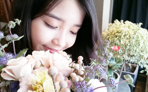 A serene HD wallpaper featuring IU, a popular Korean musician, enjoying a beautiful bouquet of flowers, set against a softly blurred background of greenery.