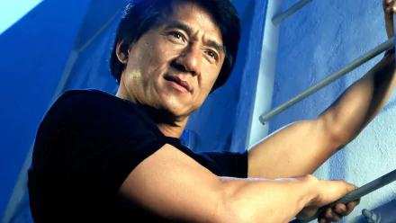 HD desktop wallpaper featuring Jackie Chan, showcasing his determined expression as he climbs a set of bars against a blue background.