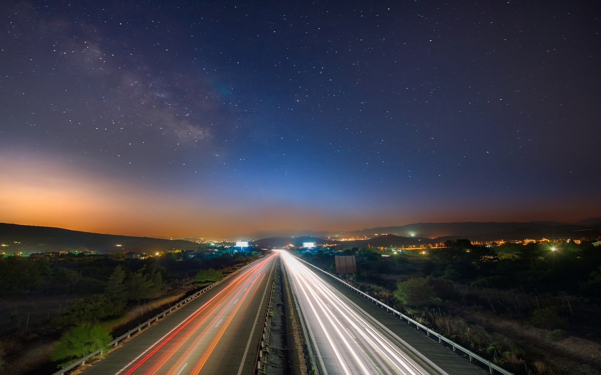 HD PC desktop wallpaper capturing a time-lapse photograph of a highway at night with streaks of car lights under a starry sky.