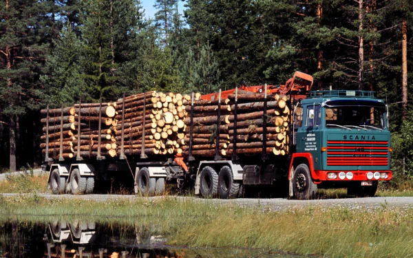 HD desktop wallpaper featuring a Scania vehicle transporting large logs through a forested area beside a reflective body of water.