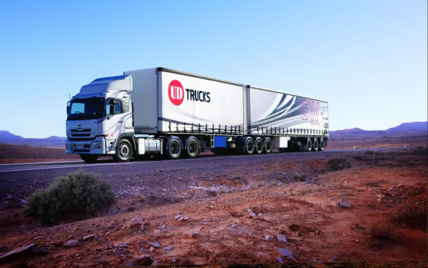 HD PC desktop wallpaper/background: UD vehicle — white UD Trucks semi-trailer rolling along a desert highway under a wide clear blue sky.