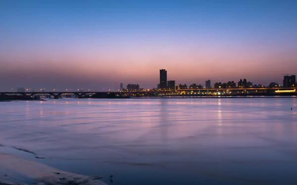 4K Ultra HD cityscape wallpaper showcasing a calm waterfront at dusk with illuminated buildings and a clear gradient sky above.