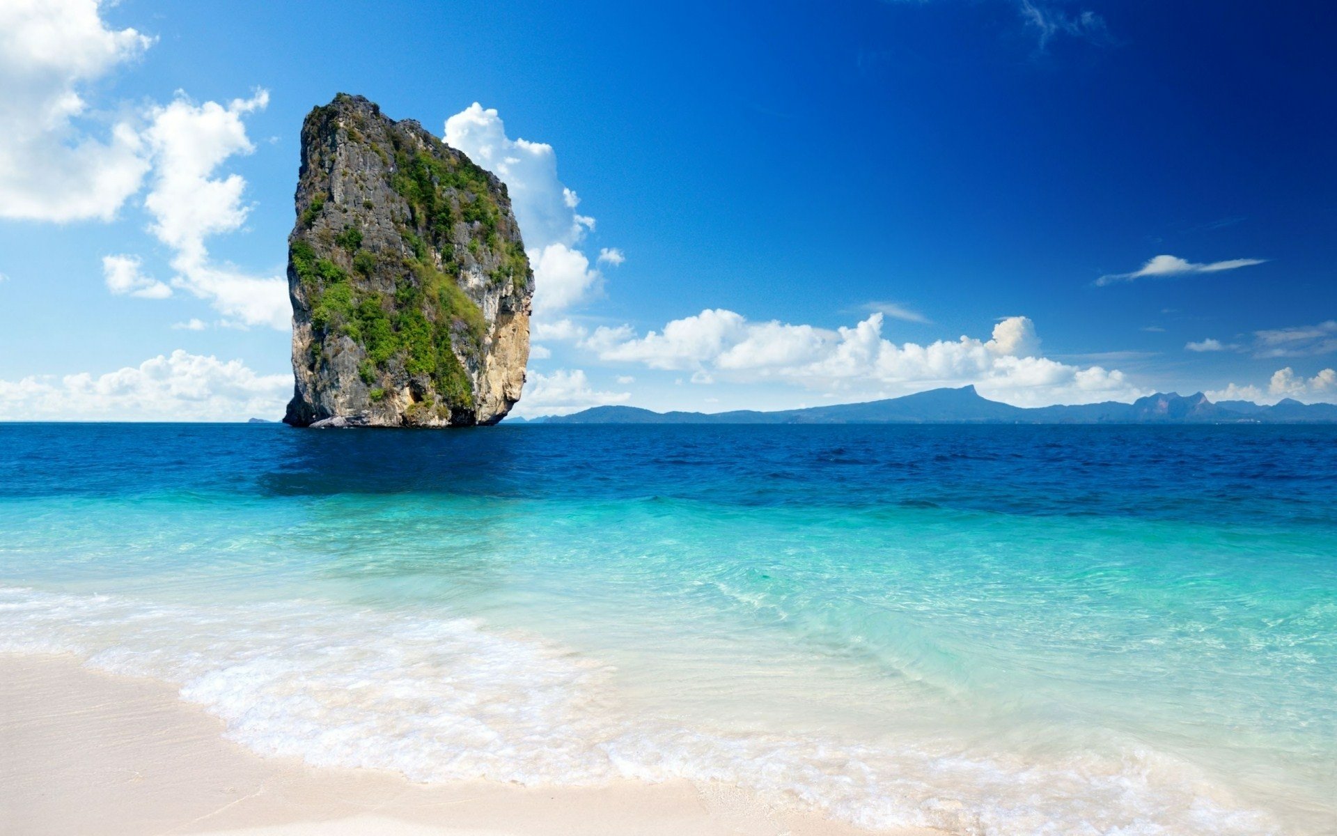 A stunning HD wallpaper showcasing a cliff rising from turquoise waters, framed by a clear blue sky and soft white sands, capturing the beauty of nature.