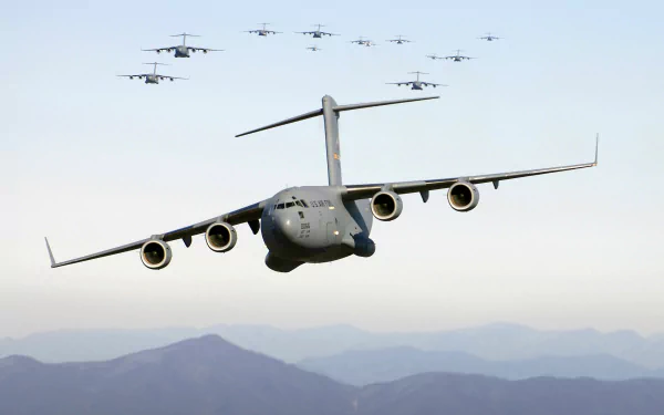 A formation of Boeing C-17 Globemaster III military transport aircraft flying over mountainous terrain, captured in an HD desktop wallpaper and background.
