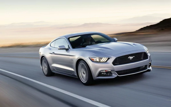A sleek 2015 Ford Mustang GT speeds along a coastal road, capturing the essence of power and style. This vibrant image serves as an HD desktop wallpaper, showcasing automotive elegance.
