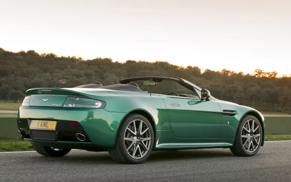 HD PC desktop wallpaper of a green Aston Martin V8 Vantage convertible parked on a roadside at sunset, shown from a rear three-quarter view.
