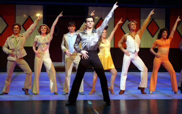 Cast of Saturday Night Fever: The Musical performing a choreographed dance number, with vibrant stage lighting, featured in a HD PC desktop wallpaper background.